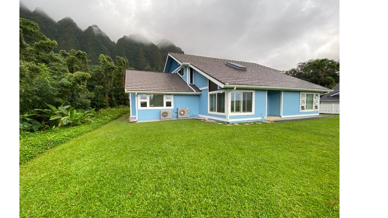 A blue house with a grey roof and a green lawn in front.